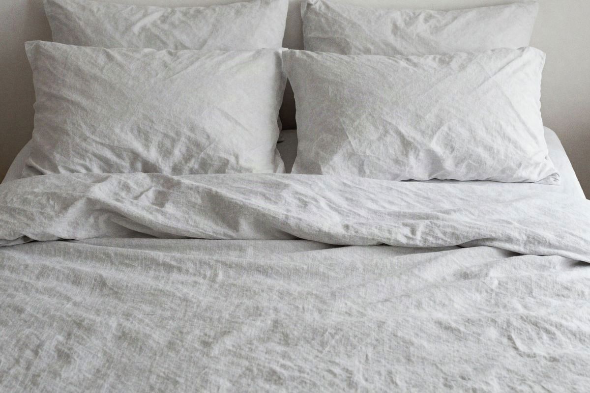 Illustrative image: bed with white linen sheets and gray pillows in a bright, peaceful bedroom
