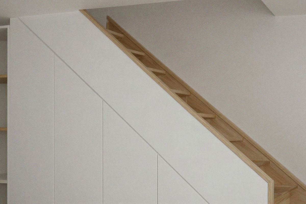 Illustrative image: Custom wooden furniture adapted to the irregular shape of the stair space.